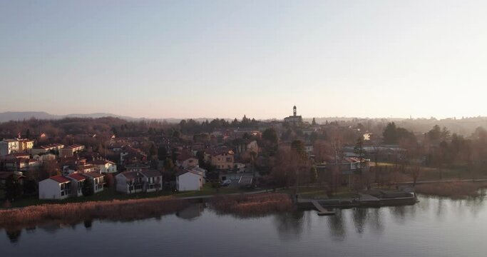 Rogeno village seen from Lake Pusiano at sunset. Aerial shot revealing houses, church and woods while camera flies up in the sky.