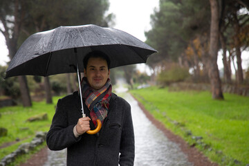 young  elegant italian  man with umbrella in the rain in the park
