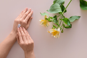 Female hands with cosmetic cream and flowers on light background