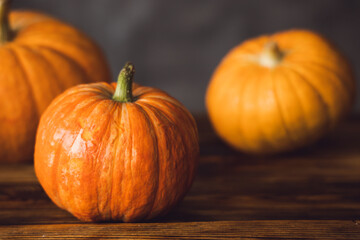 Three orange pumpkins on the brown table and grey background. Selective focus.