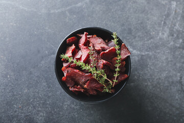 Bowl with spicy beef jerky on dark background