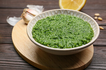 Bowl of tasty pesto sauce and ingredients on wooden background
