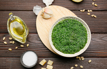 Bowl of tasty pesto sauce and ingredients on wooden background