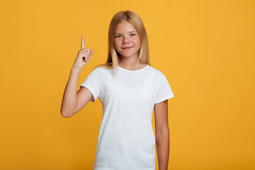Smiling confident cute teen blonde lady in white t-shirt showing thumb up to copy space