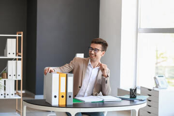 Young man with folders at table in office