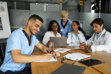 Friendly multiethnic team of doctors sitting at table, using laptop