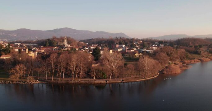 Bosisio Parini village seen from there lake at sunset in a winter day. Aerial shot with camera sliding to the left.