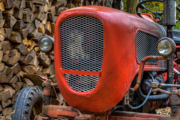 Fototapeta premium Radiator grille of an ancient, bright red tractor standing in front of a pile of fire wood in the forest..