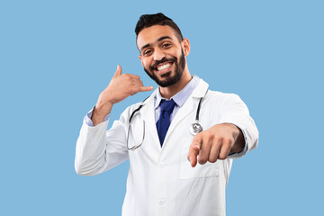 Fototapeta premium Cheerful Arab Doctor Male Gesturing Call Me On Blue Background