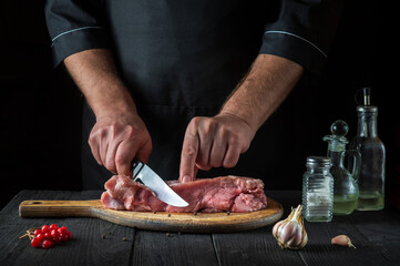 The cook cuts meat with a knife before baking. Spices on the kitchen table in a restaurant for preparing a delicious lunch.