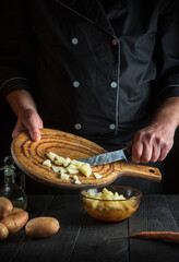 Professional chef prepares raw potatoes for lunch or dinner. Close-up of a cook hands while working in restaurant kitchen