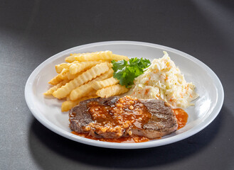 freshly grilled Sirloin Steak sauce with french fries and salad served in white dish on dark background