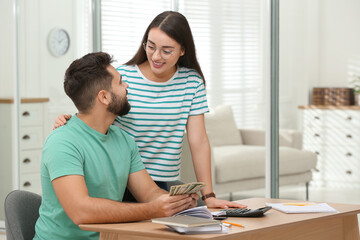 Fototapeta premium Happy young couple counting money at wooden table indoors