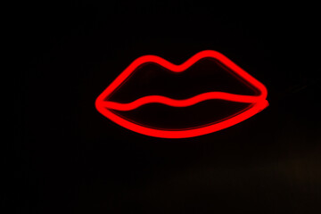 Blurry neon red lips close-up on a black isolated background.