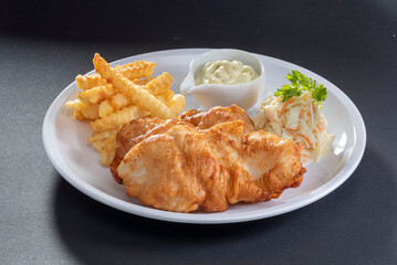 British Traditional Fish and chips with salad and tartar sauce in white dish on dark grey background top view