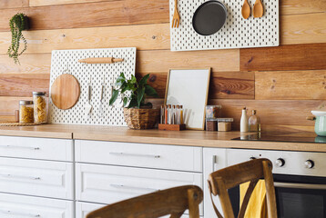 Interior of modern kitchen with white counters, peg boards and wooden wall