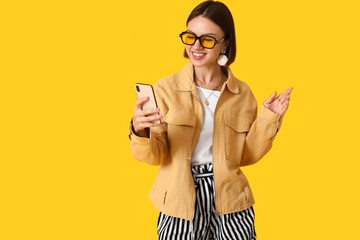 Pretty young woman in stylish clothes and with phone on color background