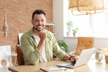Naklejka premium Handsome man working with laptop at table in office