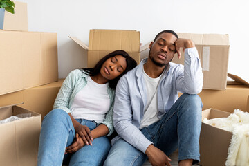 Real estate and renting issues concept. Sleepy african american couple sitting among cardboard...