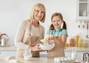 Obraz na płótnie Canvas Happy senior lady and her granddaughter preparing dough