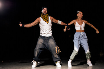 active man and woman dancing hip-hop in casual clothes on black background at dance hall with white light. Youth culture, hip-hop, movement, style and fashion, action. Fashionable portrait.