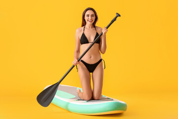Young woman with board for sup surfing and oar on color background