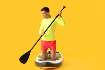 Young man with board for sup surfing and oar on color background