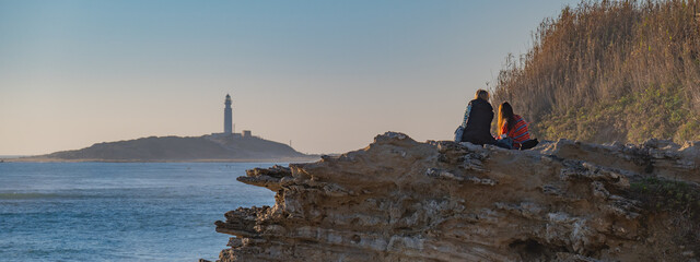 A couple watching the sunset in the Cape of Trafalgar on a rock 