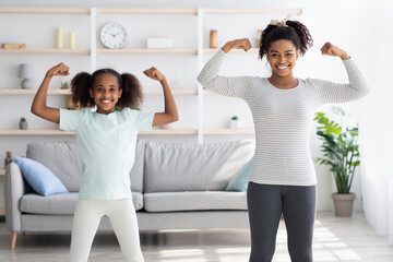 Strong afro-american mother and daughter showing their muscles