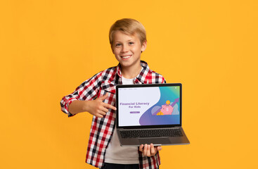 Smiling Caucasian boy pointing at laptop screen with Financial Literacy For Kids school website, orange background