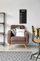 Soft armchair and to-do board hanging on light wall in room