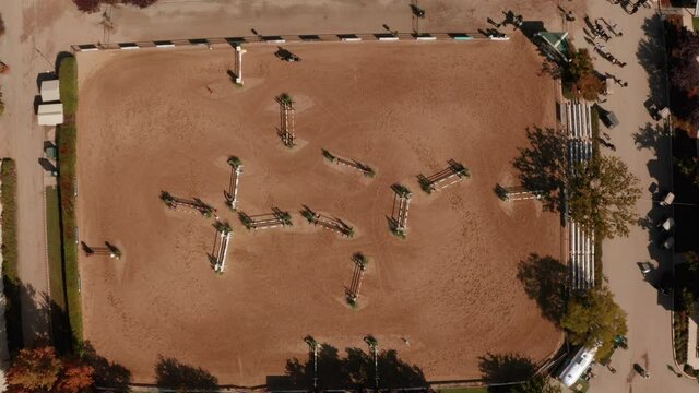 Top down aerial view over a show jumping course as a rider and horse jump the obstacles.