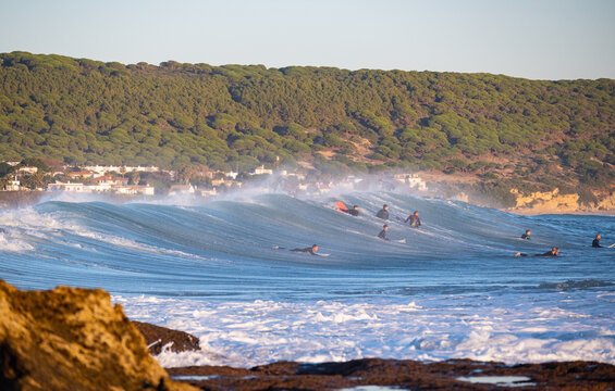 Surfers passing over huge wave next to la Bre&ntilde;a cliffs in Barbate