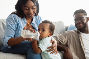 Happy African American mom feeding child from bottle