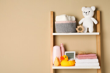 Towels, toys and baby accessories on wooden rack, space for text
