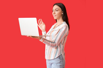 Young woman with modern laptop on red background