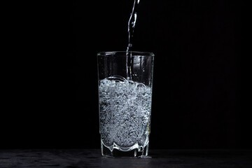 Mineral water is poured into a glass on a black background. Useful drinking mineral water.