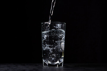 Mineral water is poured into a glass on a black background. Useful drinking mineral water. - obrazy, fototapety, plakaty
