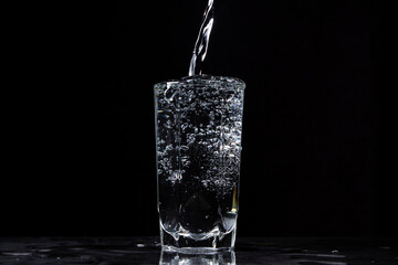 Mineral water is poured into a glass on a black background. Useful drinking mineral water.