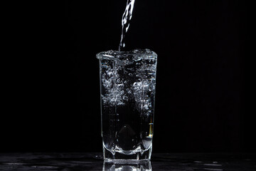 Mineral water is poured into a glass on a black background. Useful drinking mineral water.