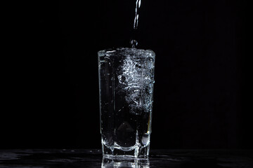 Mineral water is poured into a glass on a black background. Useful drinking mineral water.