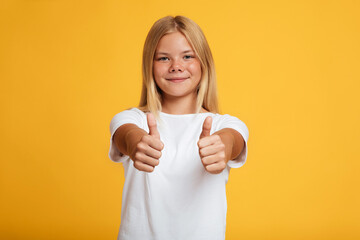 Cheerful teenager blonde girl in white t-shirt showing thumbs up gesture, rejoice to excellent mark