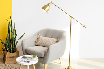 Golden standing lamp, armchair and table near light wall