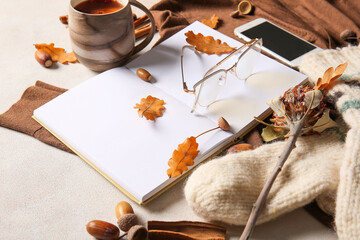 Blank book, cup of tea, mobile phone, eyeglasses and autumn decor on light background