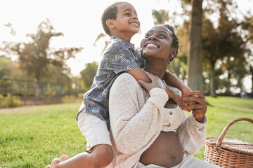 African pregnant mother and son hugging together at city park - Family love