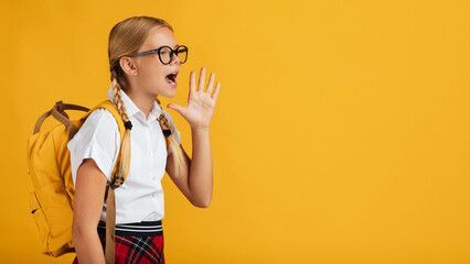 Funny teenager blonde girl pupil with pigtails, backpack in glasses shouts at free space