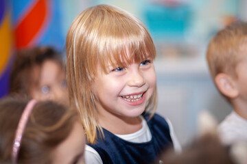 A happy girl on a holiday, a close-up portrait of a child, a laughing girl, blond hair, a beautiful smile in a baby.
