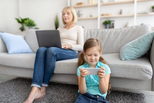Mature woman and granddaughter using laptop and cell phone