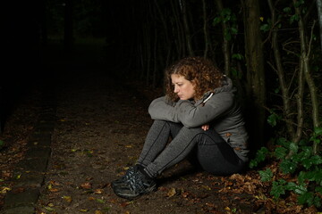 Frau sitzt im dunklen Wald, nachdenklich und deprimiert, Kopf auf die Arme gestützt