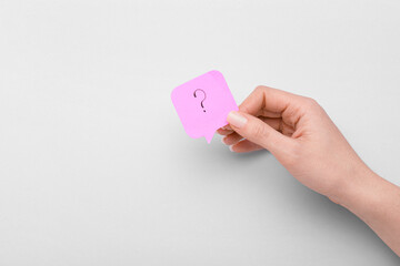 Woman holding sticky note with question mark on light background